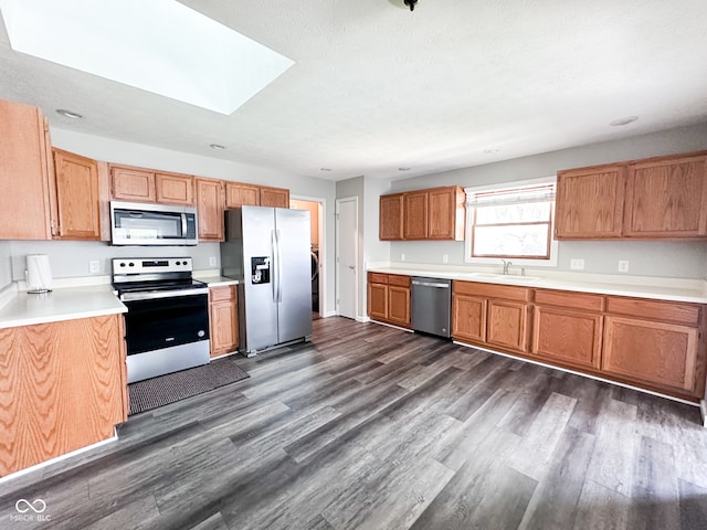 kitchen featuring appliances with stainless steel finishes, sink, dark wood-type flooring, and a skylight