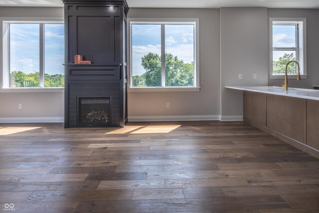 unfurnished living room with a wealth of natural light, a fireplace, sink, and dark hardwood / wood-style floors