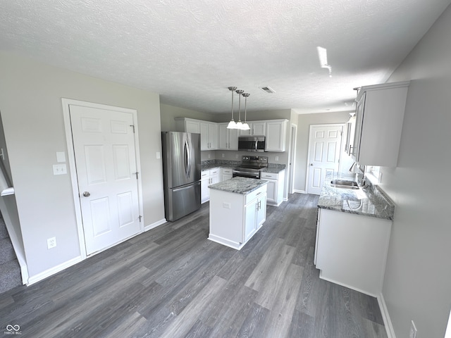 kitchen featuring appliances with stainless steel finishes, sink, a kitchen island, dark wood-type flooring, and hanging light fixtures