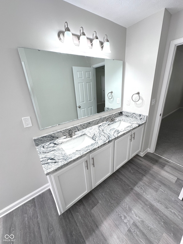 bathroom featuring a textured ceiling, hardwood / wood-style floors, and dual bowl vanity