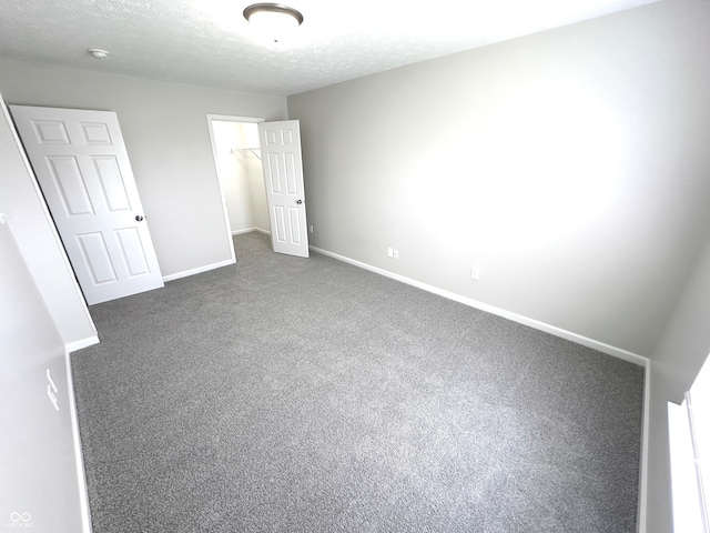 unfurnished bedroom featuring carpet, a closet, a textured ceiling, and a spacious closet