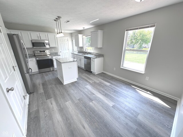 kitchen with sink, appliances with stainless steel finishes, light hardwood / wood-style floors, a kitchen island, and pendant lighting