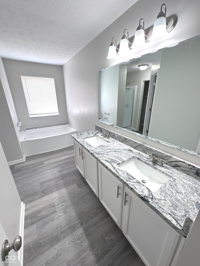 bathroom featuring a tub, hardwood / wood-style floors, a skylight, a textured ceiling, and double sink vanity