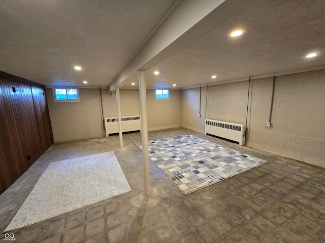 basement featuring a textured ceiling, radiator, and light tile patterned flooring