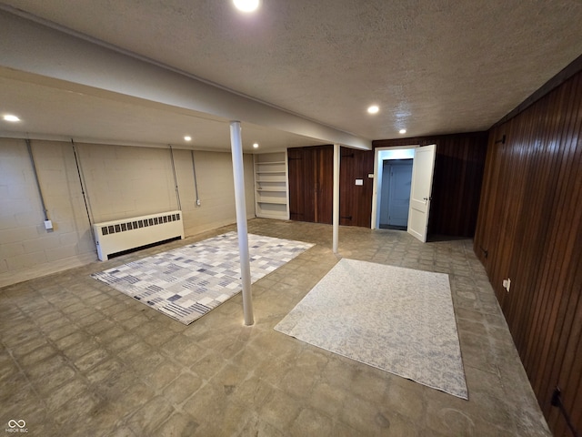 basement with wood walls, light tile patterned flooring, a textured ceiling, and radiator