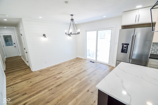 kitchen with high end refrigerator, light hardwood / wood-style flooring, light stone countertops, a chandelier, and white cabinets