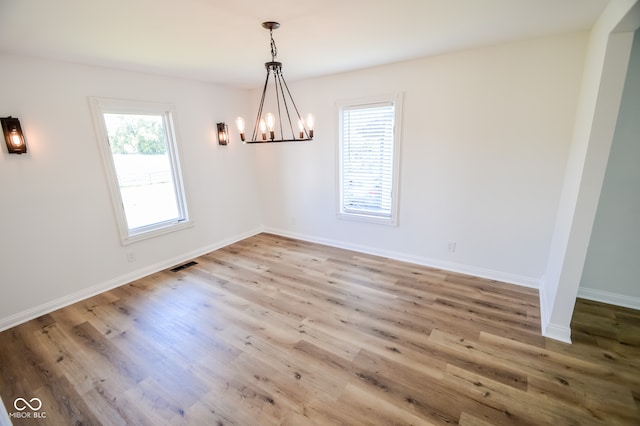 unfurnished dining area with a notable chandelier and hardwood / wood-style flooring