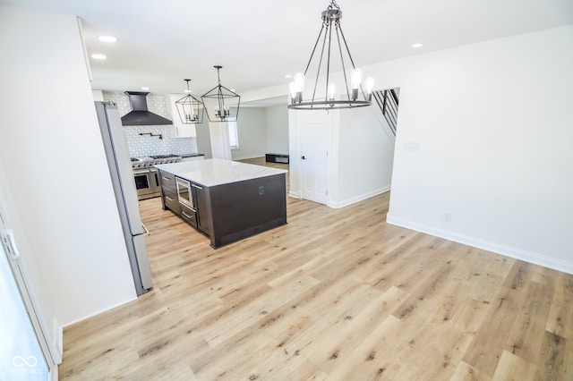 kitchen featuring appliances with stainless steel finishes, light hardwood / wood-style floors, decorative backsplash, wall chimney range hood, and a center island