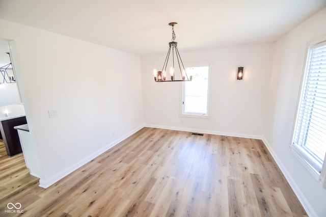 unfurnished dining area with a notable chandelier and light hardwood / wood-style flooring