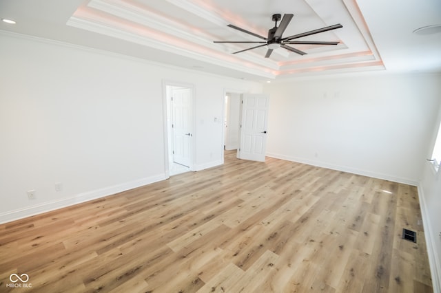 empty room with ceiling fan, a raised ceiling, crown molding, and light hardwood / wood-style floors