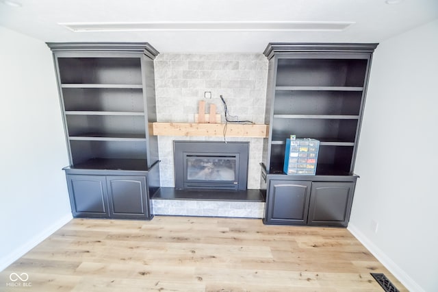 unfurnished living room with light wood-type flooring, built in shelves, and a fireplace