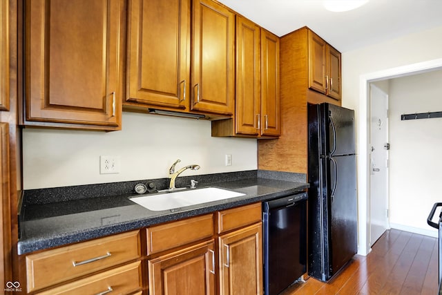 kitchen with sink, black appliances, wood-type flooring, and dark stone counters