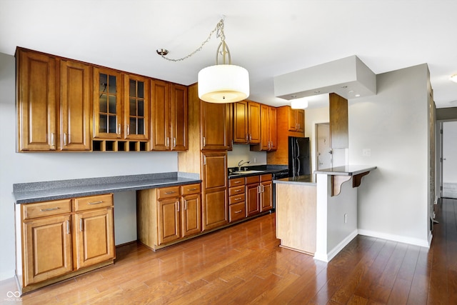 kitchen with sink, hanging light fixtures, black refrigerator, and wood-type flooring