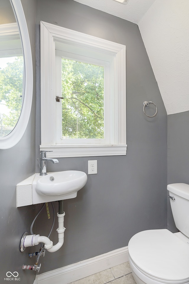 bathroom with lofted ceiling, toilet, sink, and tile patterned flooring