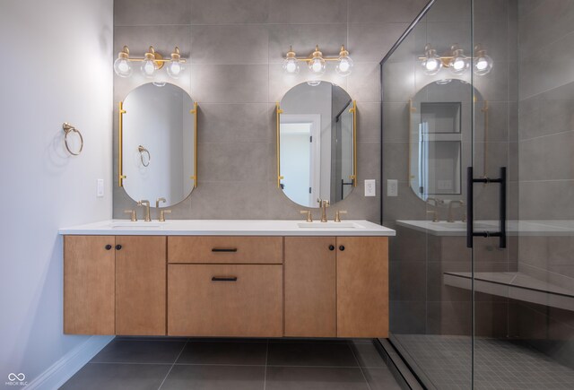 bathroom with a shower with door, dual bowl vanity, tile patterned flooring, and tile walls