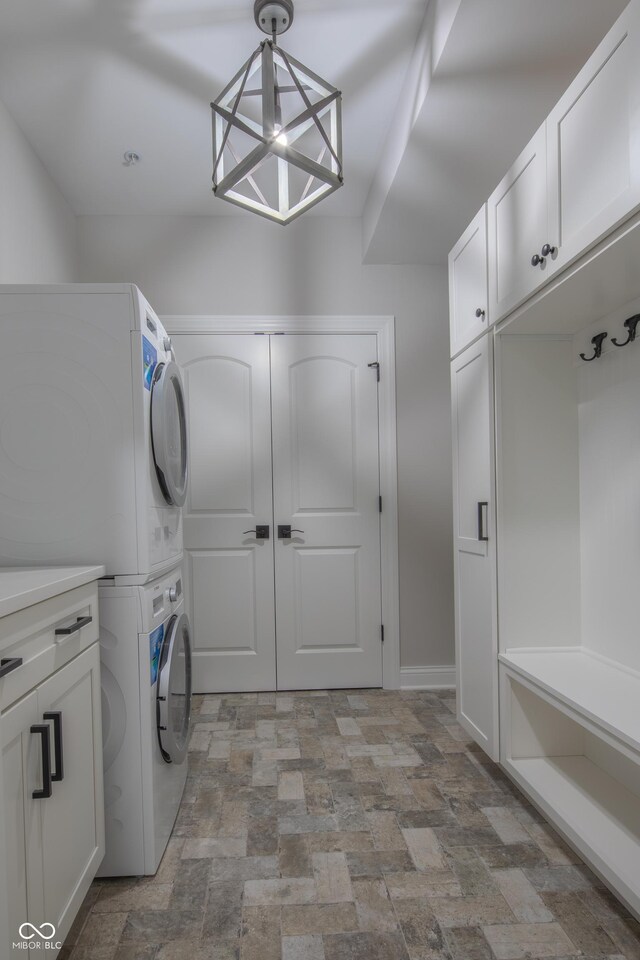 washroom with a chandelier, cabinets, and stacked washer / dryer