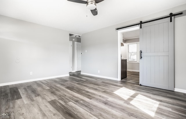 unfurnished bedroom featuring a ceiling fan, a barn door, baseboards, and wood finished floors