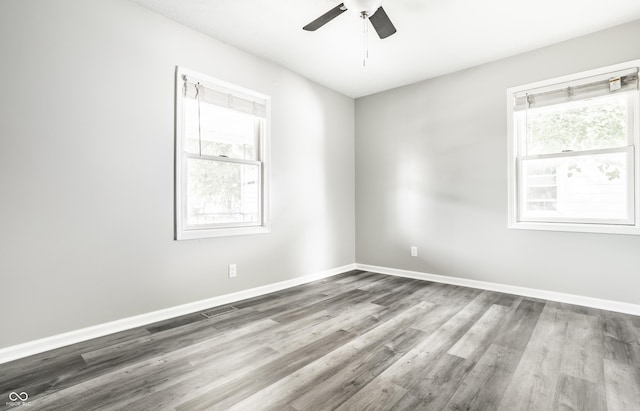 spare room featuring a ceiling fan, visible vents, baseboards, and wood finished floors