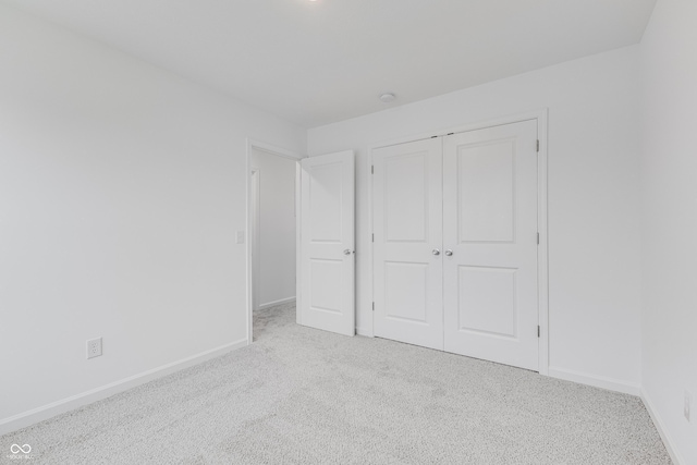 unfurnished bedroom featuring light carpet, baseboards, and a closet