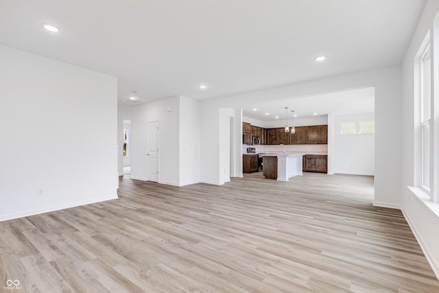 unfurnished living room featuring baseboards, light wood finished floors, a sink, and recessed lighting