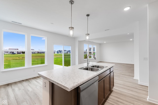 kitchen featuring a center island with sink, a sink, light countertops, pendant lighting, and stainless steel dishwasher