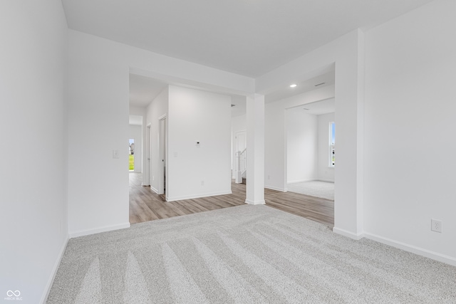 empty room featuring stairway, baseboards, and light colored carpet