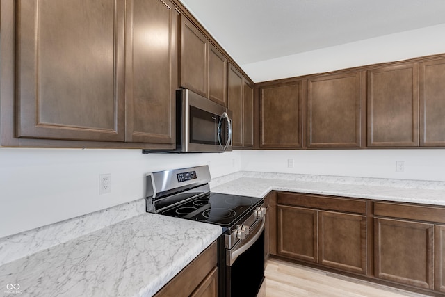 kitchen with appliances with stainless steel finishes, light wood-type flooring, dark brown cabinetry, and light stone countertops