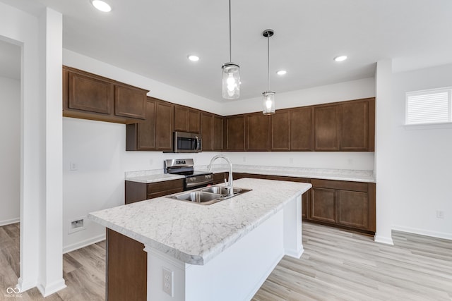 kitchen featuring hanging light fixtures, a kitchen island with sink, stainless steel appliances, light countertops, and a sink