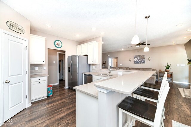 kitchen featuring backsplash, dark wood-type flooring, hanging light fixtures, appliances with stainless steel finishes, and kitchen peninsula