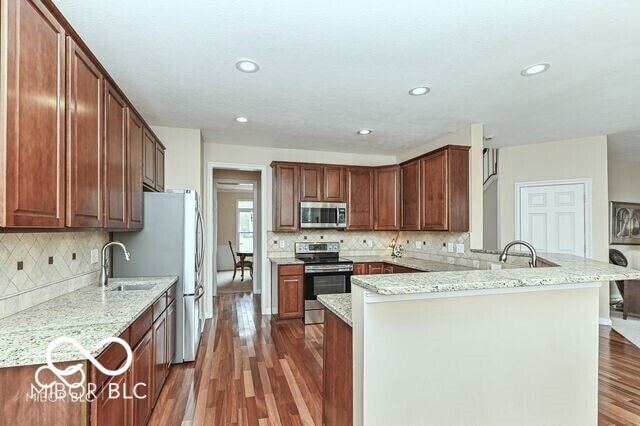 14626 Warner Trl, Westfield, IN 46074 - kitchen with appliances with stainless steel finishes, a peninsula, a sink, wood finished floors, and decorative backsplash