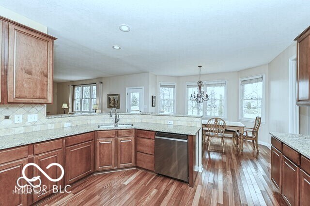 14626 Warner Trl, Westfield, IN 46074 - kitchen featuring stainless steel dishwasher, a sink, wood finished floors, light stone countertops, and a peninsula