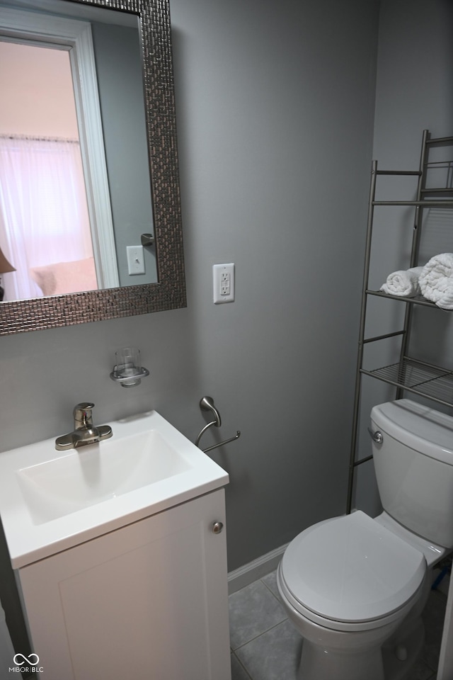 half bath with toilet, tile patterned floors, baseboards, and vanity