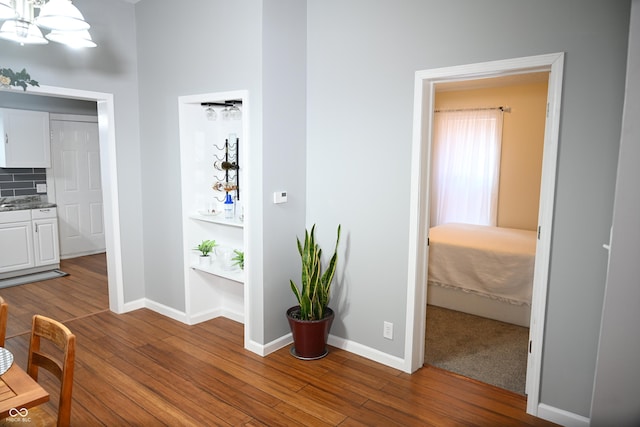 hall with an inviting chandelier, baseboards, and wood finished floors