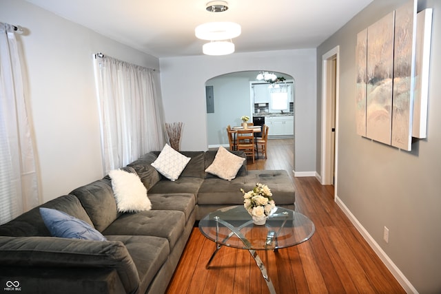 living area with baseboards, electric panel, arched walkways, and wood finished floors