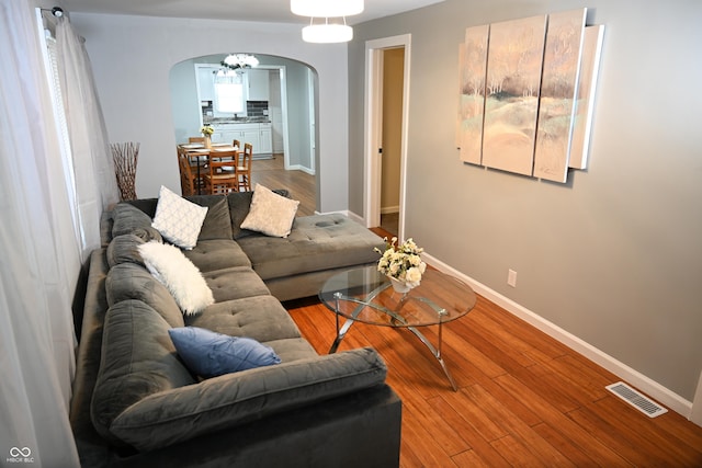 living area with arched walkways, wood finished floors, visible vents, and baseboards