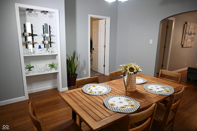 dining space featuring arched walkways, dark wood finished floors, and baseboards