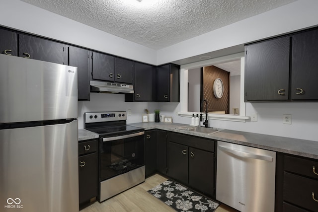 kitchen featuring appliances with stainless steel finishes, a textured ceiling, light hardwood / wood-style floors, and sink