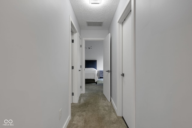 hall with a textured ceiling and light colored carpet