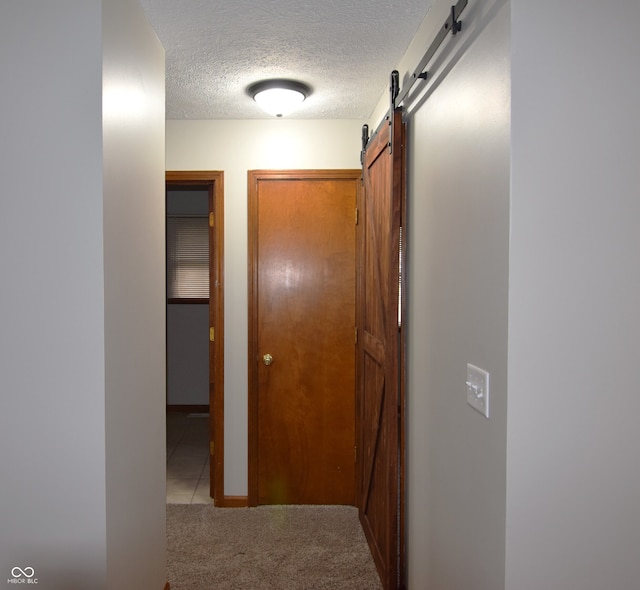 hall with a barn door, a textured ceiling, and light carpet