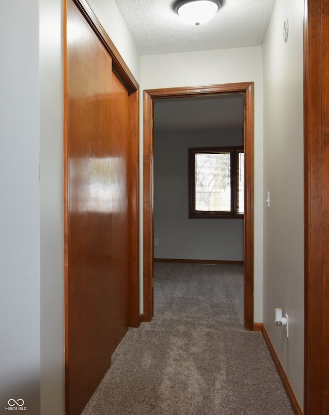 corridor featuring a textured ceiling and dark colored carpet