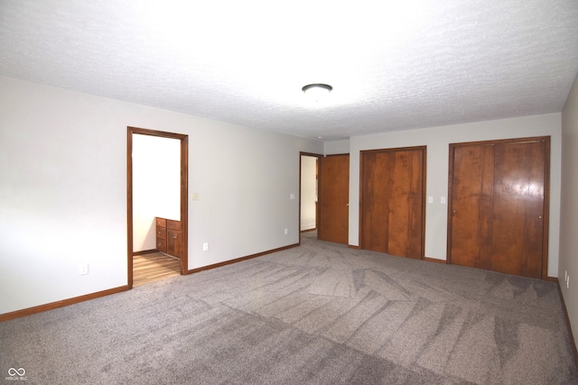 unfurnished bedroom featuring a textured ceiling, connected bathroom, light colored carpet, and multiple closets