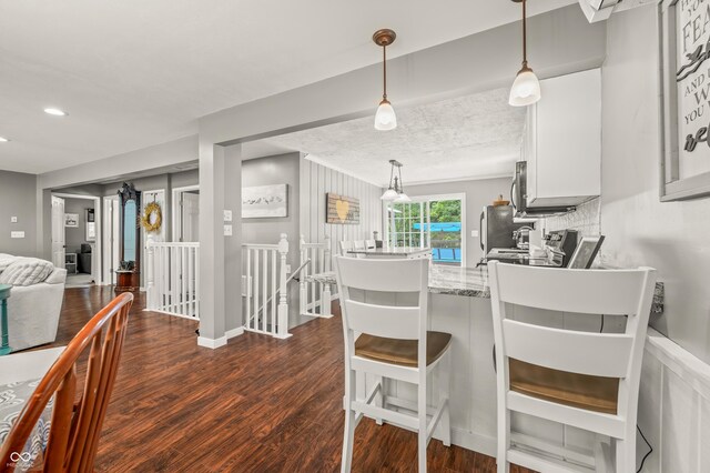 kitchen featuring decorative backsplash, dark hardwood / wood-style floors, white cabinetry, a breakfast bar area, and kitchen peninsula