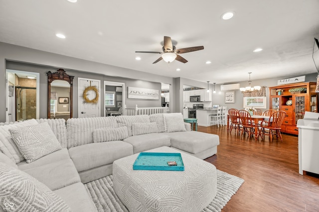 living room featuring ceiling fan with notable chandelier, a wall mounted AC, and wood-type flooring