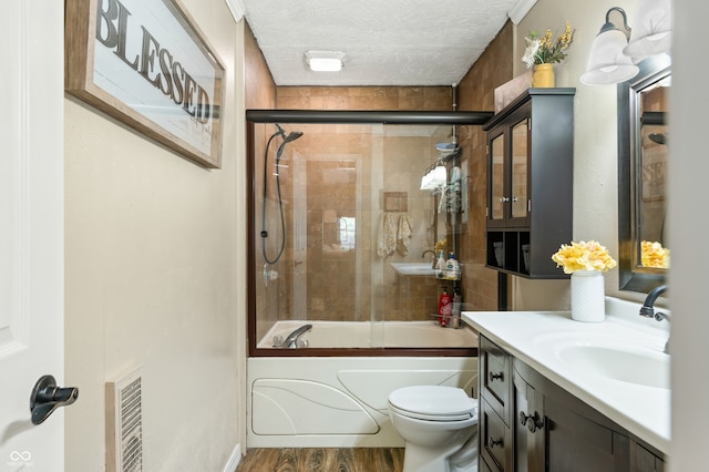 full bathroom with hardwood / wood-style flooring, a textured ceiling, vanity, bath / shower combo with glass door, and toilet