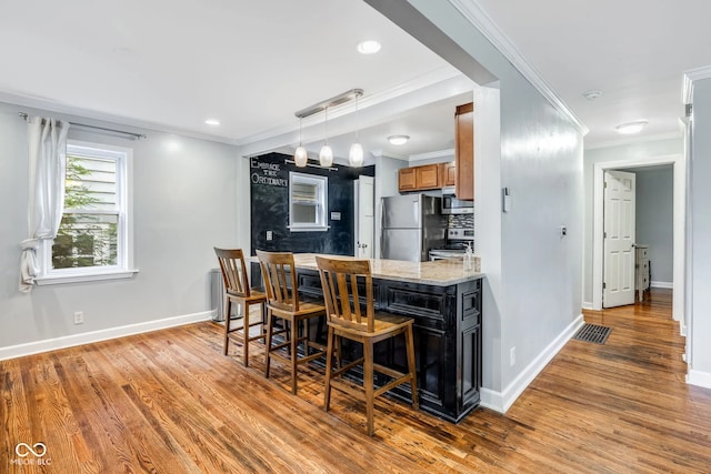 kitchen with light hardwood / wood-style floors, stainless steel refrigerator, crown molding, pendant lighting, and stove