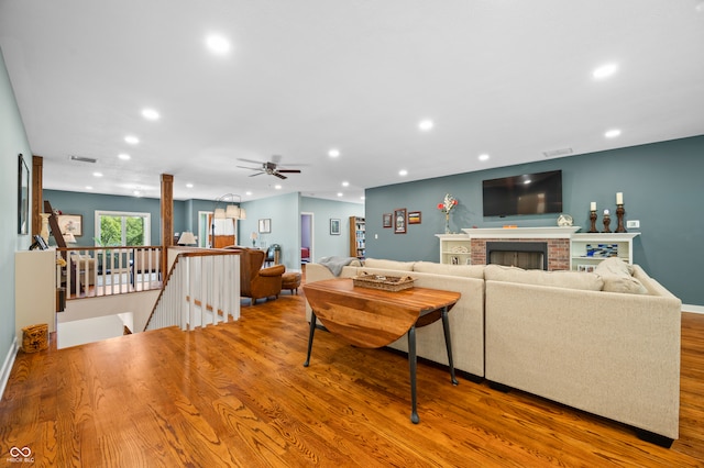 living room with ceiling fan, a brick fireplace, and hardwood / wood-style flooring