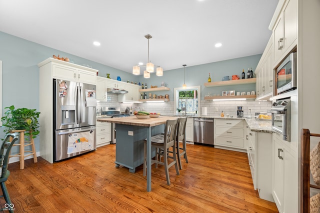 kitchen with a kitchen breakfast bar, appliances with stainless steel finishes, a center island, butcher block counters, and white cabinets