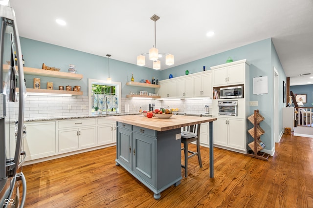 kitchen featuring pendant lighting, butcher block countertops, a kitchen island, appliances with stainless steel finishes, and white cabinets