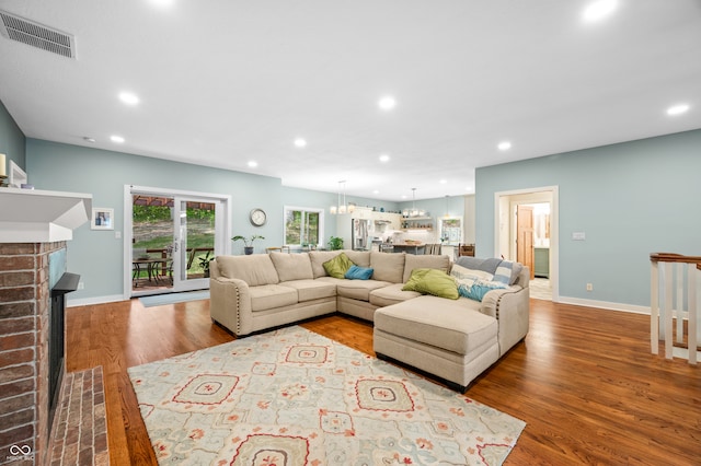 living room with a chandelier, a brick fireplace, and hardwood / wood-style flooring