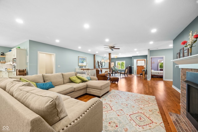 living room with ceiling fan, hardwood / wood-style floors, and a brick fireplace